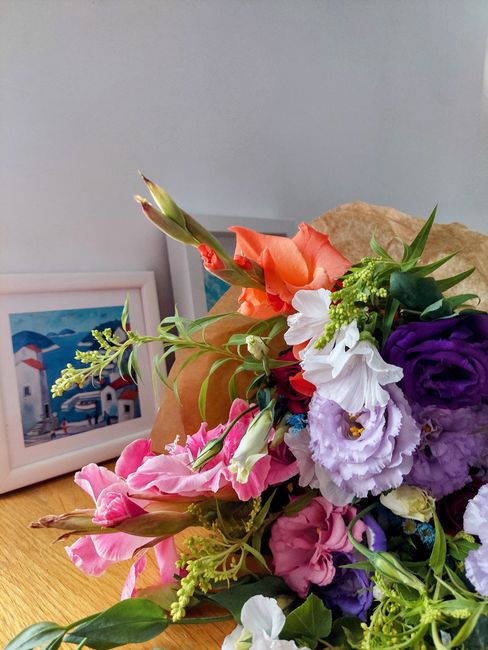 A vibrant bouquet of fresh flowers featuring a variety of blooms including pink, purple, white, and orange flowers. The arrangement includes lisianthus, delphiniums, and gladiolus, with green foliage 