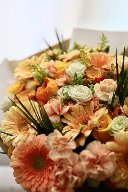 A floral bouquet featuring a variety of fresh flowers including peach gerbera daisies, creamy white roses, soft pink lisianthus, and pale yellow roses, all arranged with green foliage and long, slende