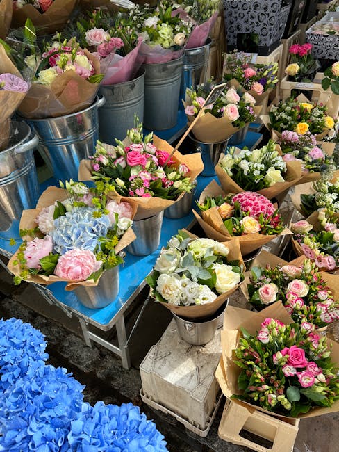 A display of various floral arrangements and bouquets on a blue table, featuring a mix of fresh flowers including pink roses, white lilies, blue hydrangeas, and other colourful blooms, all wrapped in 